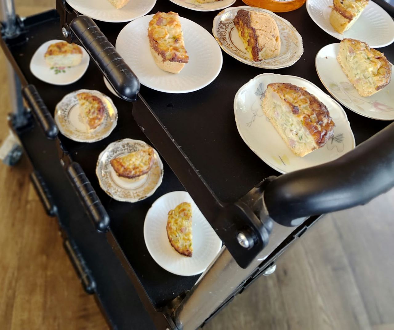 Servierwagen mit vielen Stücken Zwiebelkuchen auf Tellern mit Goldrand und Blümchenmuster