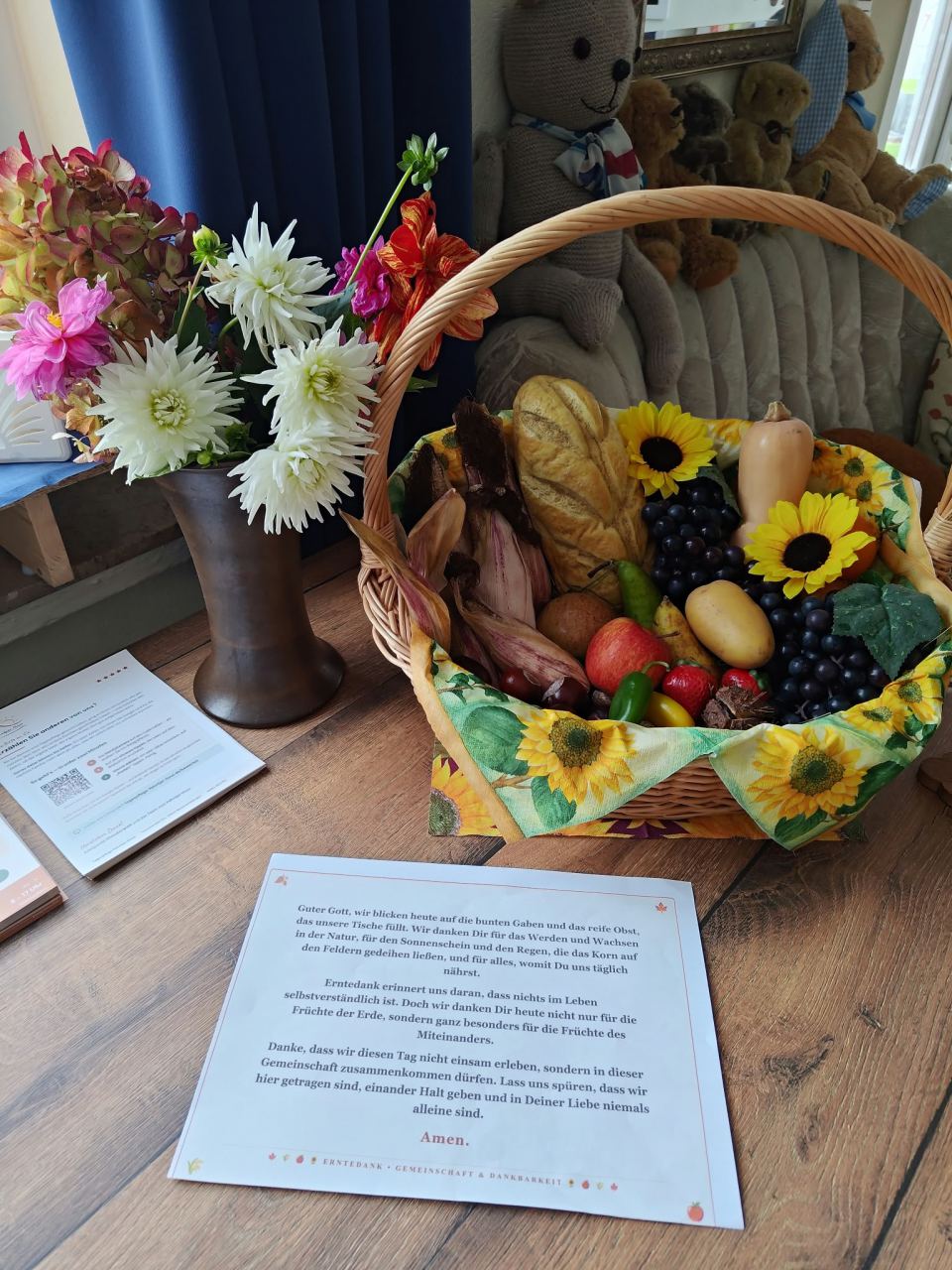 Erntekorb mit Brot, Kürbis, Obst, Maiskolben und Sonnenblumen, daneben ein Herbststrauß und ein Erntedank-Gebet