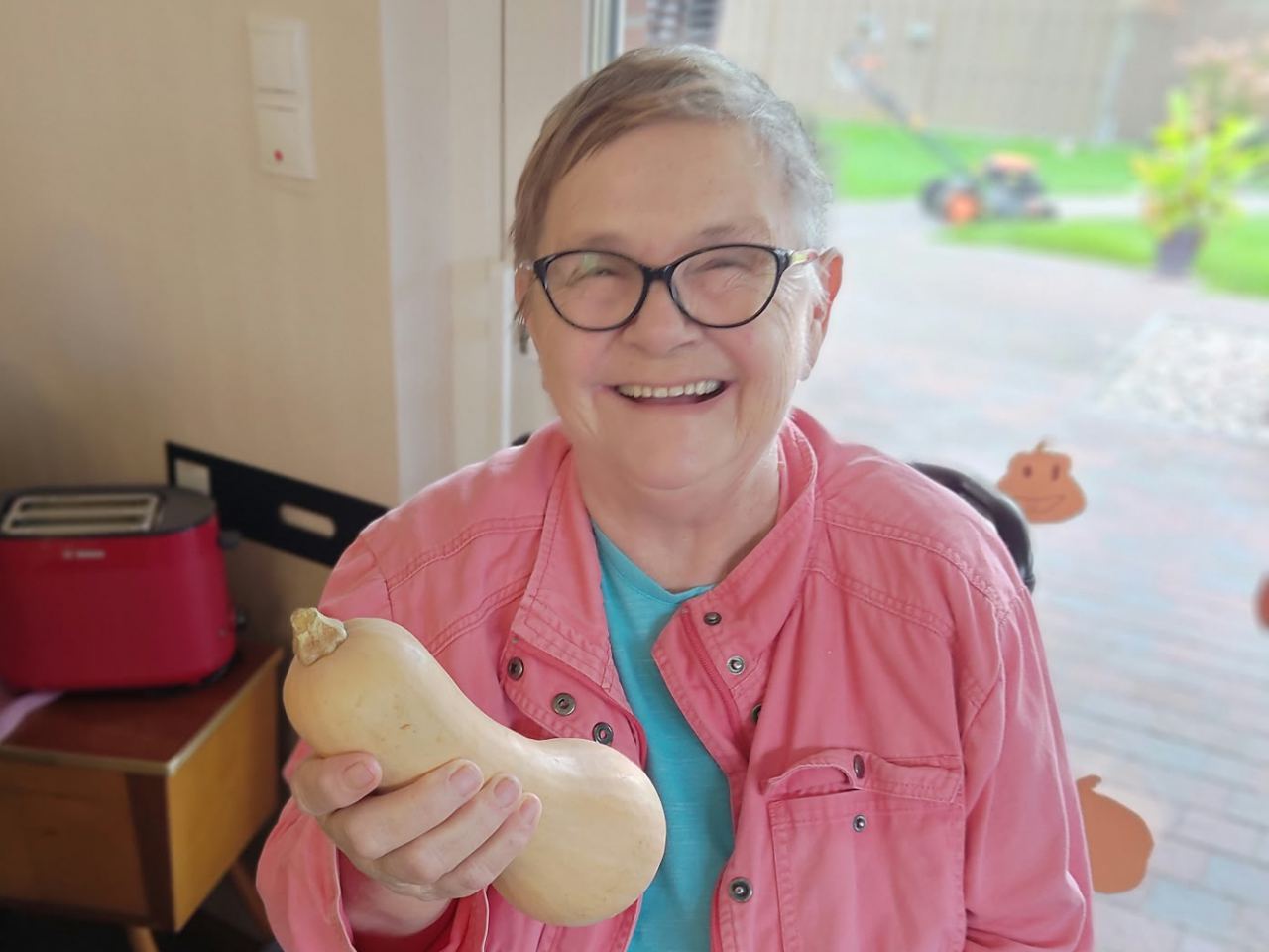 Eine lachende Seniorin hält einen Butternut-Kürbis in die Kamera