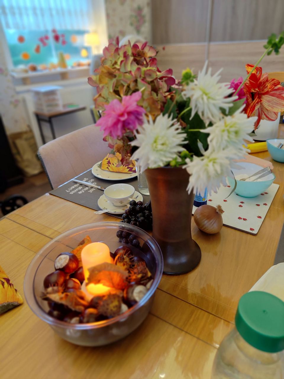 Herbstlich gedeckter Tisch mit Kastanien im Kerzenlicht, Weintrauben, Herbstblumen und einer Zwiebel